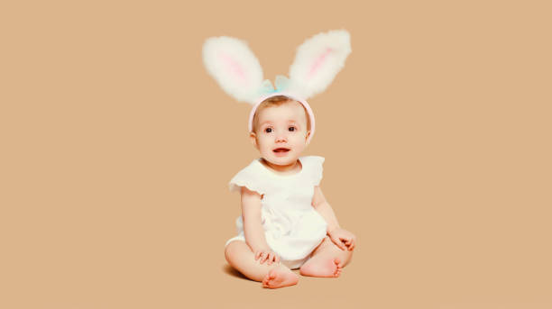 istock Portrait cute baby with easter rabbit ears sitting on brown studio background 2151418569