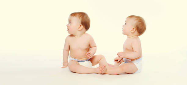 istock Two twin babies in diapers sitting on the floor on white studio background 2151418784