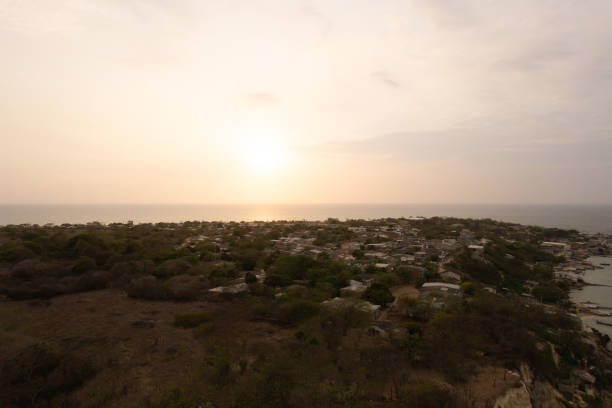 Aerial view of a coastal village at sunset, with the sun casting a warm glow over the rooftops and the sea in the background.