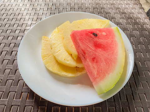 Pineapple and watermelon slices on a white plate, outdoor setting.