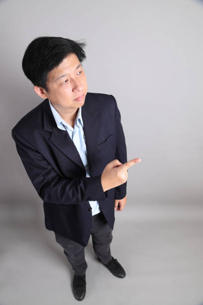 The Asian Businessman with formal dressed with gesture of pointing on the gray background.