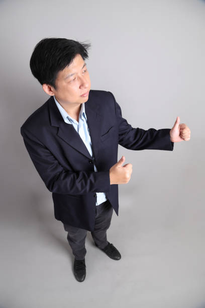 The Asian Businessman with formal dressed with gesture of thumbs up on the gray background.
