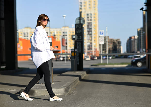 Young woman in formal clothes walking near grey wall outdoors, space for text