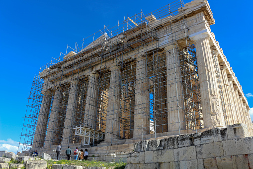 Athens, Greece - March 13, 2024: Amidst scaffolding and bustling activity, the Parthenon, an enduring symbol of classical architecture, undergoes meticulous restoration. Skilled craftsmen and engineers work tirelessly to preserve the magnificence of this ancient marvel, carefully repairing weathered marble and reinforcing delicate columns. Despite the construction, the timeless elegance of the Parthenon still shines through, its majestic silhouette standing as a testament to the ingenuity and resilience of ancient civilizations. As visitors observe the ongoing restoration efforts, they are reminded of the enduring legacy and cultural significance of this iconic monument.