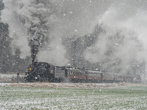 A train is traveling through a snowy field. The steam from the train is visible in the air, creating a sense of movement and energy. The scene evokes a feeling of adventure and excitement