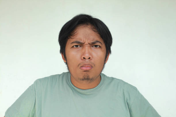 Close up of young Asian man with annoyed expression. Isolated in gray background.
