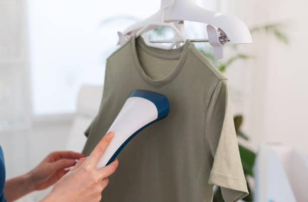 istock Using steaming iron to ironing t-shirt in home. Doing stream vapor iron for press clothes in hand. 2151448157