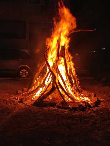 The picture depicts a big a bonfire that is crackling at night, with beautiful orange and yellow flames all around.