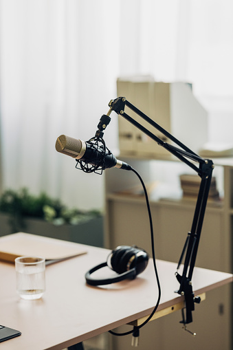 A professional podcast setup on a desk featuring a studio microphone with pop filter and a pair of headphones, set against a modern office background.