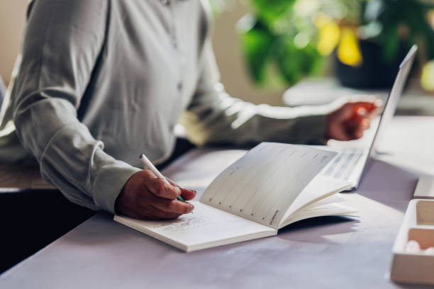 Business Professional Writing in Notebook Beside Laptop