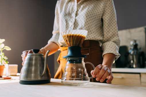 A focused woman elegantly prepares hand-poured coffee in a sunlit modern kitchen, demonstrating a popular brewing method.