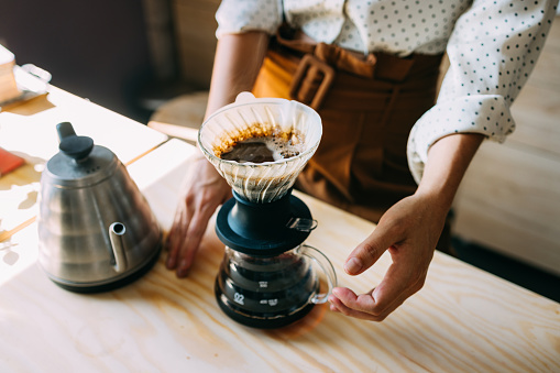 A skilled barista pours hot water over freshly ground coffee in a pour over brewer, showcasing expertise in a vibrant cafe atmosphere.