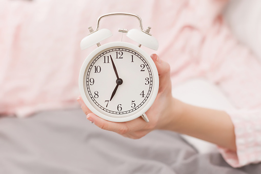 White clock and a woman in pink pajamas sleeping on the bed