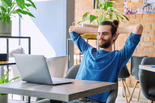 istock Satisfied relaxed young man looking at laptop screen while sitting in coworking cafe 2151460448