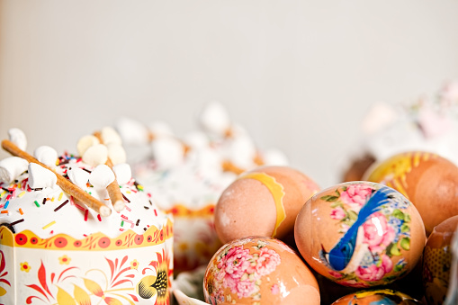 Easter cake with protein glaze, sugar sprinkles, marshmallow on top and eggs decorated with patterns, on a with blurred background. Orthodox Easter in eastern Europe. Vertical photo