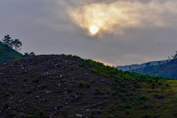 A dramatic landscape with rolling hills, some barren and others covered in a patchwork of green vegetation, bathed in the warm light of the setting sun in Wahniangleng, Meghalaya.