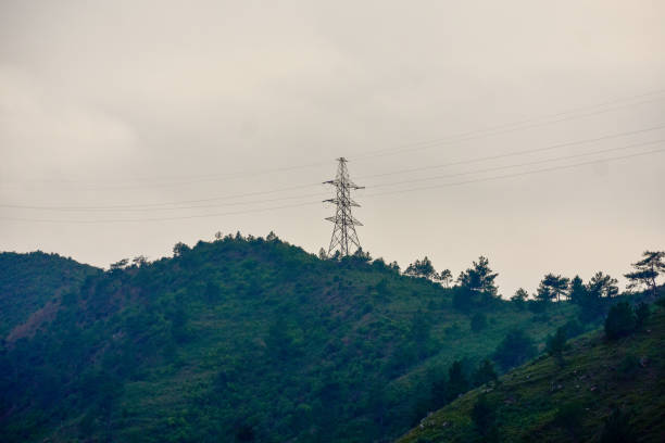 A lone power transmission tower standing tall on a hilltop. High-voltage cables stretch from the metallic structure, carrying electricity across the hilly landscape in Meghalaya.