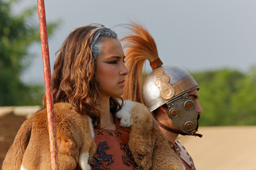 Aquileia, Italy - June 22 2014: Close-up of a beautiful caucasian young girl seen in profile and next to a soldier at the historical reenactment of the battle between the ancient Romans and the Carnic Gauls