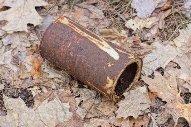 one large brown rusty iron tin can stands on gray dry leaves and earth on the street
