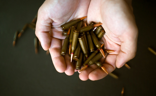 Male hands hold a handful of ammunition, cartridges in his hands on the dark background, close-up view. The concept is about war, the army and complex conflicts with the economic crisis.