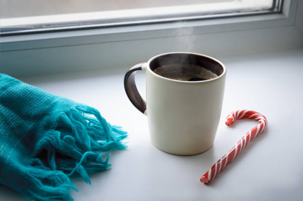 There is a mug of hot coffee on the windowsill. Nearby lies a turquoise scarf and a lollipop.