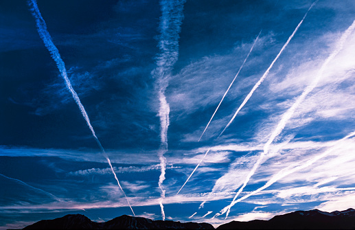 View of the Sierra Nevada mountain range, looking east, under a sky filled with jet airplane contrails (vapor trails) caused by jet aircraft engine exhaust.