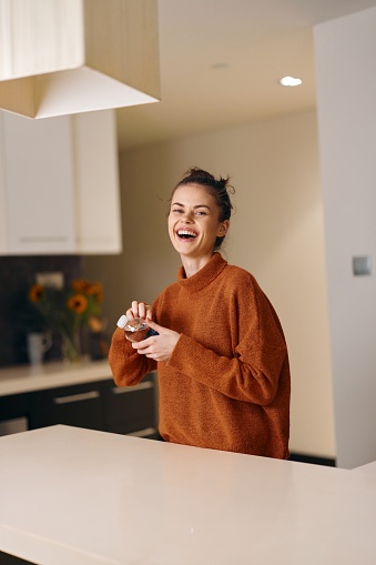 Happy Woman, a Portrait of a Cheerful and Attractive Young Female in a Modern Caucasian Home Kitchen, Smiling and Holding a Cup of Healthy Tea, Enjoying a Positive Morning with Natural Beauty and Confidence, Surrounded by a Casual White Interior and Technology