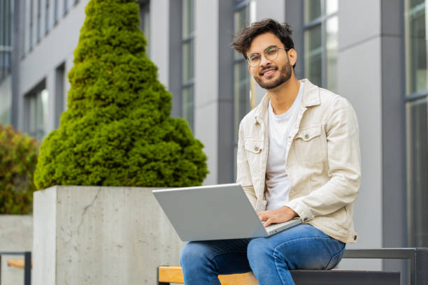 istock Indian man freelancer working on laptop computer sends messages reading email outdoors on bench 2151484206