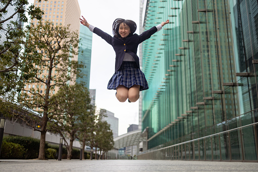 Teenage girl in school uniform jumping in city