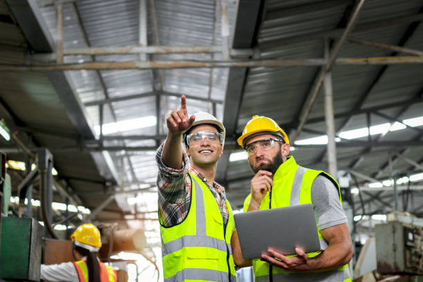 istock Industrial foreman and worker with helmet and safety vest using laptop computer during discussing together at manufacturing industry factory. Engineer inspecting workplace and checking process. 2151507327