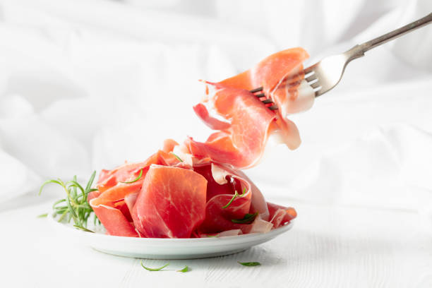 Prosciutto with rosemary on a white wooden table.