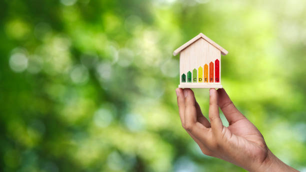 istock Concepts for evaluating energy efficiency in homes. Human hand holding a model house model and energy saving charts in home models On a Green background. 2151520509
