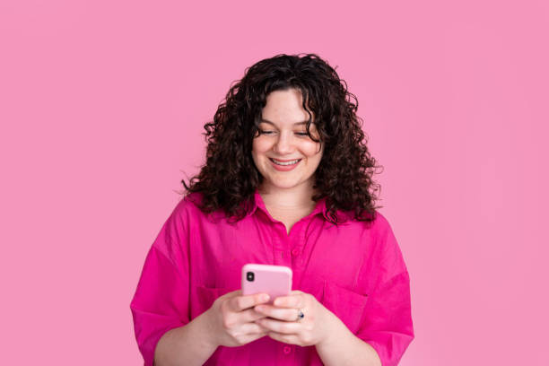 istock Smiling young woman with smartphone on pink background 2151523867