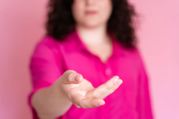 Close-up image of an outstretched hand of a woman in a pink shirt with selective focus on pink background