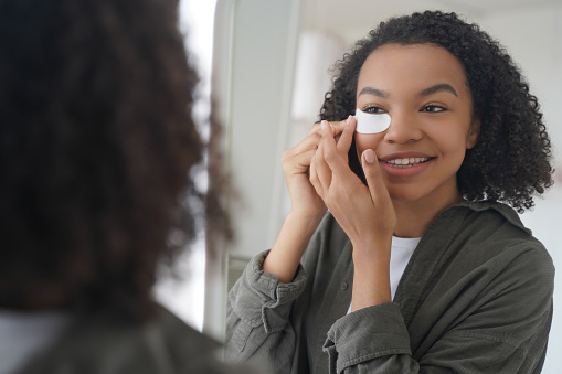 A radiant young woman applies a beauty product, smiling at her reflection.