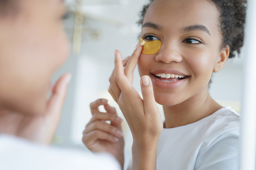 Person happily applies eye patches, indulging in a skincare routine and enjoying a beauty treatment.