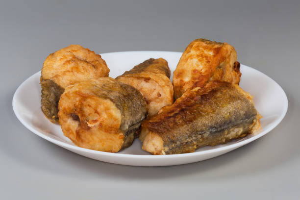 Fried pieces of hake hubbsi, or Argentine hake on white dish on a gray background, side view close-up