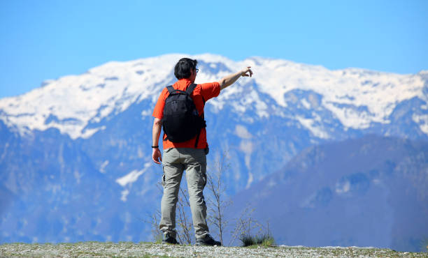 istock young Man hiker with backpack standing on a mountain trail looking at snowcapped peaks 2151530155