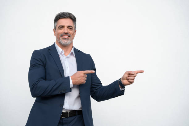 istock Smiling mature 40s old grey haired businessman in formal suit, pointing both hands at copy space for promo advertising. Businessman standing and point isolated on white background, looking camera 2151530254
