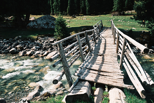 Old wooden footbridge over stream in mountain forest