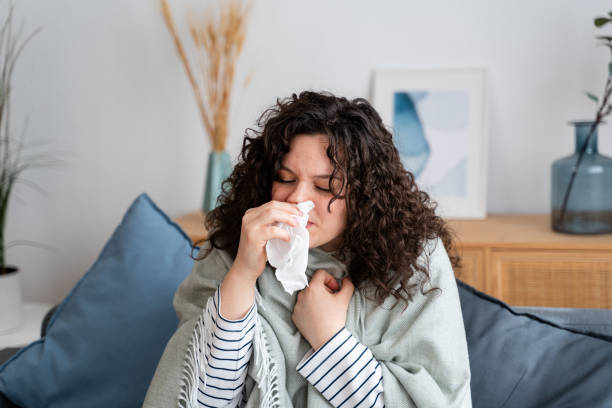istock Sick woman blowing nose while resting on couch at home 2151539420