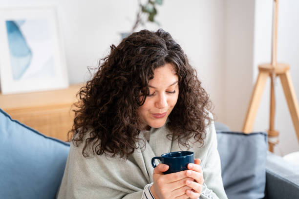 istock Cozy home relaxation - woman enjoying a warm drink on a comfortable sofa 2151539509