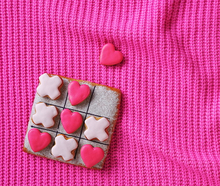 Bright Pink Wallpaper for Valentine's day. A tic-tac-toe game made of gingerbread. On the background of a knitted Sweater Texture