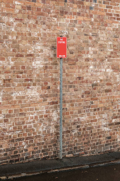 Red metal No stopping sign on a gray metal pole, with a brick wall behind.