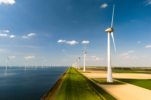 A row of elegant wind turbines stand tall next to a serene body of water, harnessing the power of the wind to generate renewable energy in the Netherlands