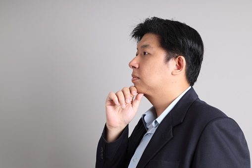 The Asian Businessman with formal dressed with gesture of thinking on the gray background.