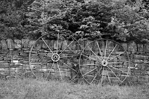 Two old metal cart wheels lean against a dry stone wall, showcasing the enduring legacy of traditional craftsmanship. Weathered by time, they symbolise resilience and the timeless wisdom of past generations. The dry stone wall, crafted without mortar, stands as a testament to enduring bonds and steadfastness against the elements. Together, they form a tableau of tradition, reminding us of the enduring values that anchor us amidst change.