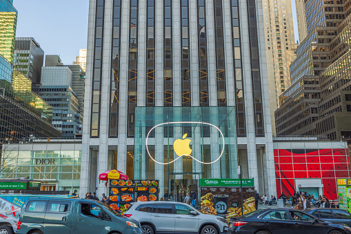 New York. USA. 05.05.2024. View of Apple Store on Fifth Avenue in New York, featuring iconic glass facade with large Apple logo, surrounded by busy city traffic and neighboring high-end stores.