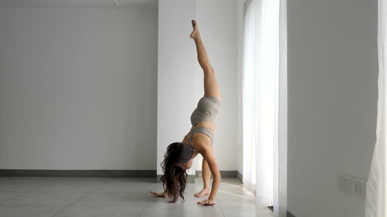 Young woman practicing yoga with a standing split pose in a bright room, morning light