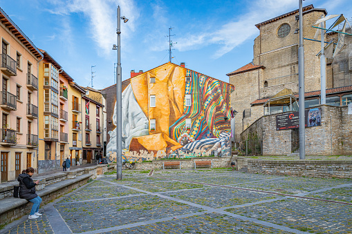 April 24th, 2024. Vitoria, Spain.  A part of the old town with one woman on the phone and a colorful mural in the background.